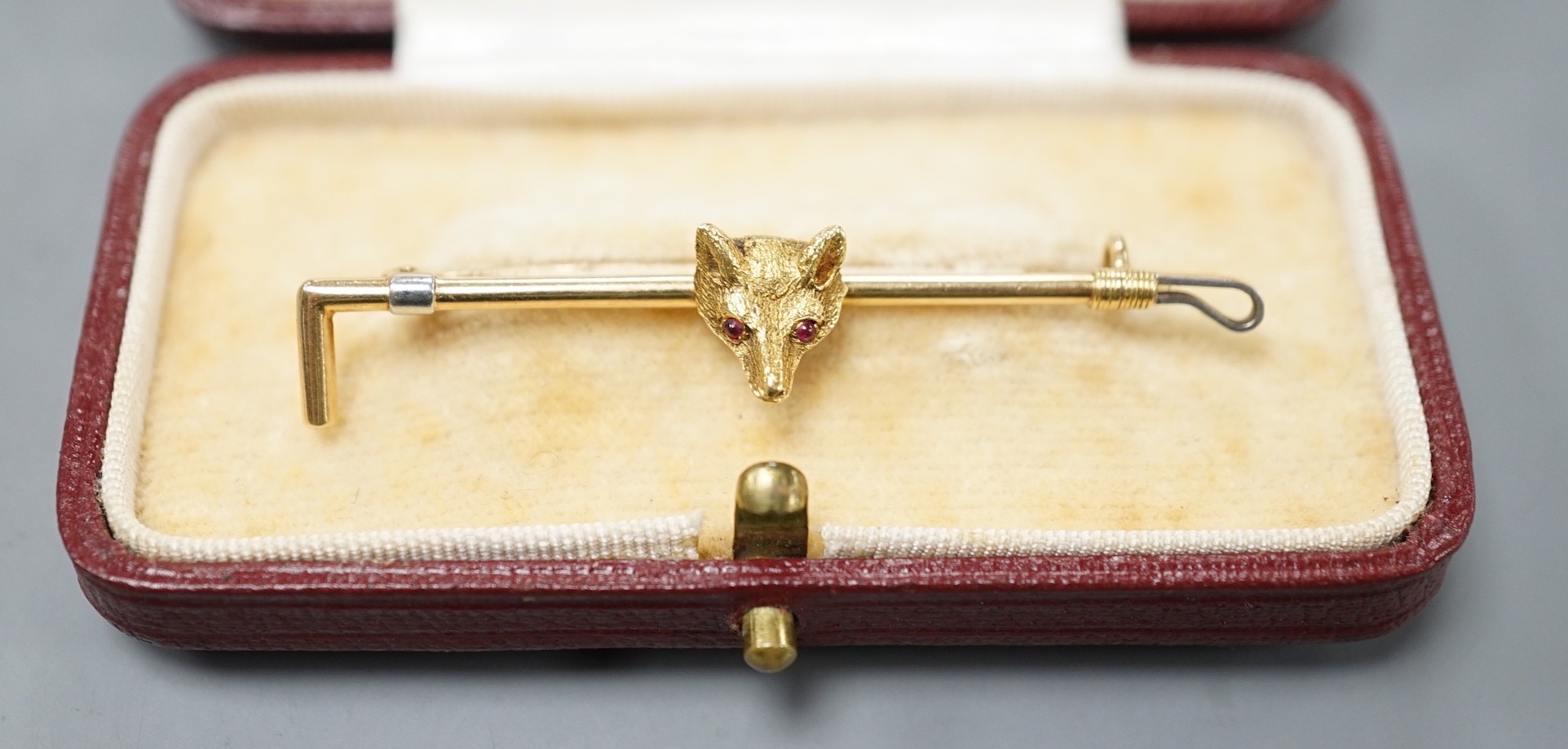 An 18ct and gem set fox head and riding crop bar brooch, 50mm, gross weight 4 grams.
